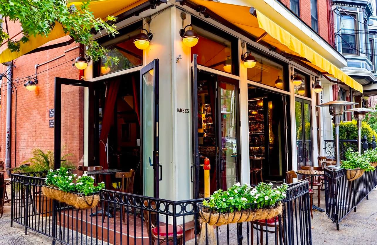 Barbès corner storefront with yellow awnings, open doors and a fenced sidewalk patio